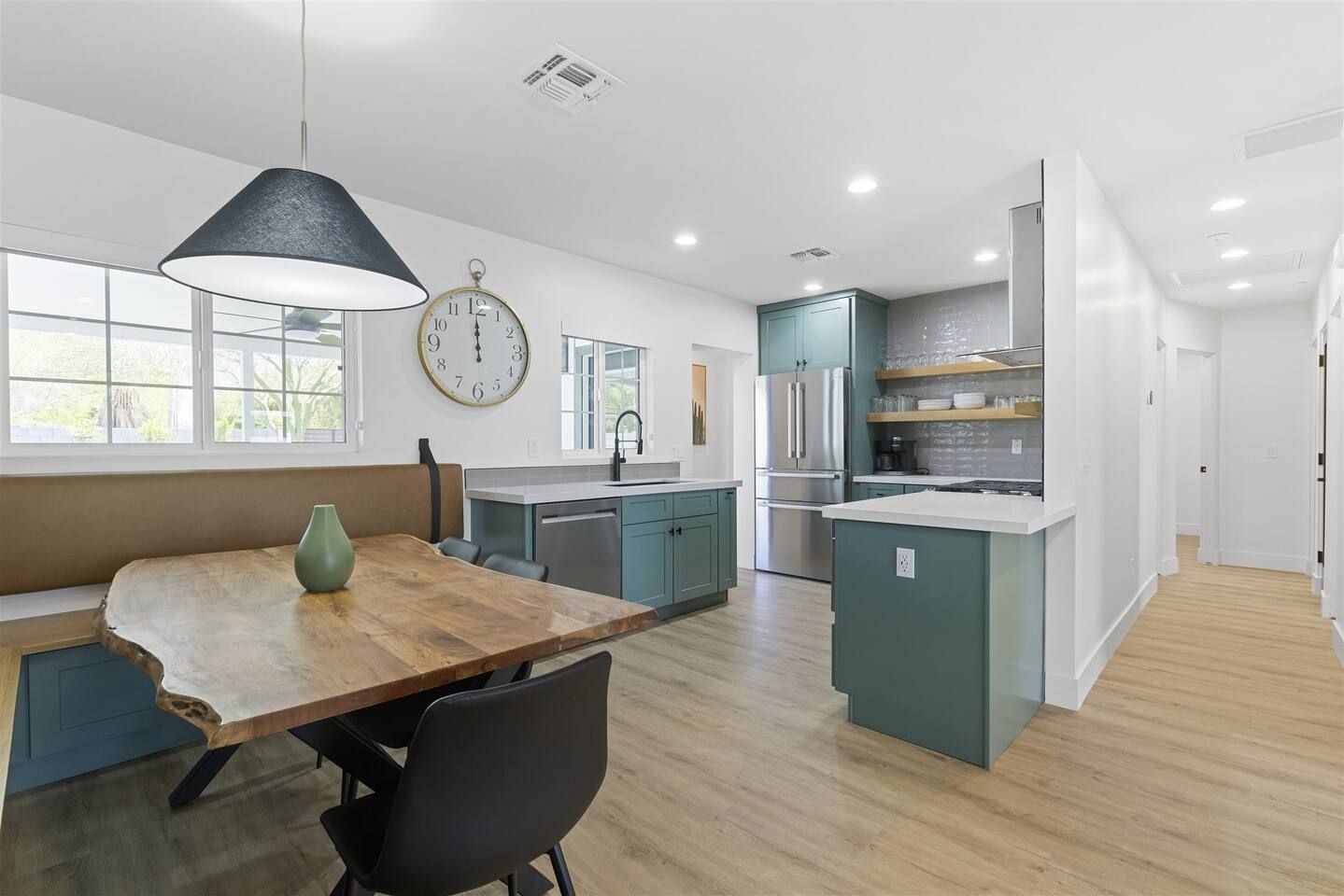 A modern kitchen with a wooden dining table, a clock, and teal cabinetry.