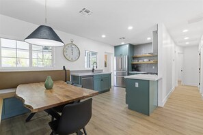 A modern kitchen with a wooden dining table, a clock, and teal cabinetry. - The Elliott at Biltmore | Fire Pit, Grill (Phoenix)
