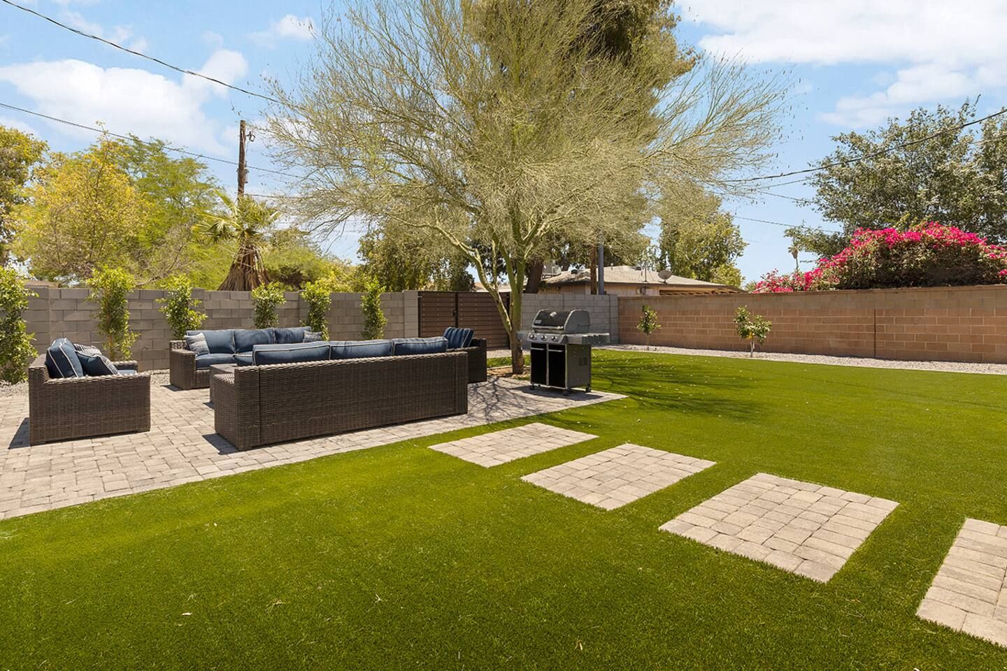 A backyard with a patio area, a grill, and a lawn.