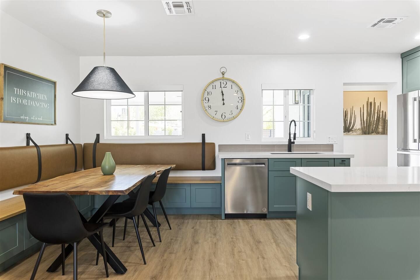 A modern kitchen with a wooden dining table, black chairs, a large clock, and a dishwasher.
