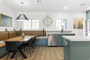 A modern kitchen with a wooden dining table, black chairs, a large clock, and a dishwasher. - The Elliott at Biltmore | Fire Pit, Grill (Phoenix)