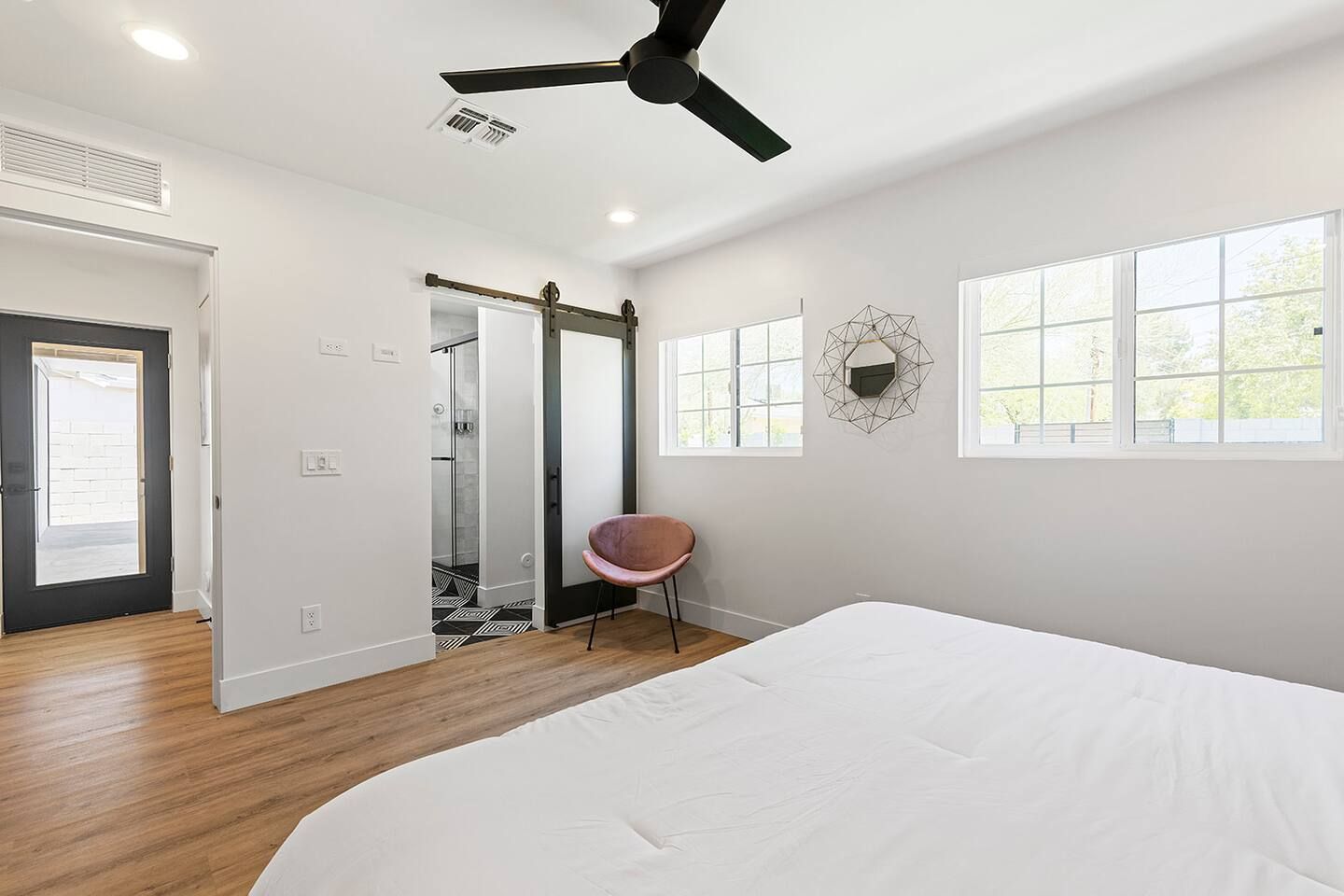 A bedroom with a bed, a ceiling fan, a shower, and a door leading to another room.