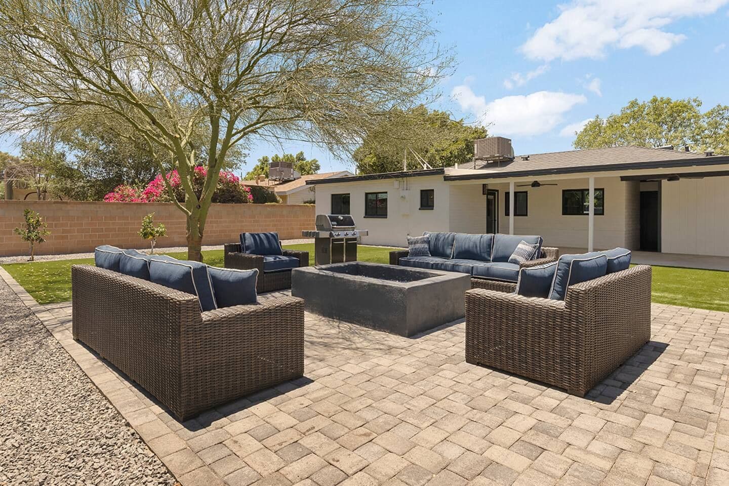 An outdoor patio with wicker furniture, a barbecue grill, and a well-maintained lawn.