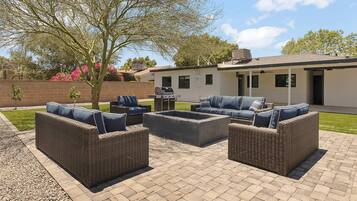 An outdoor patio with wicker furniture, a barbecue grill, and a well-maintained lawn.