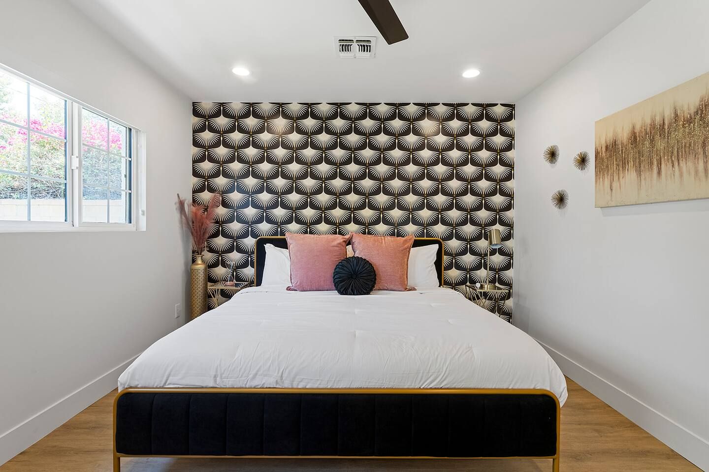 A bedroom with a bed, a patterned headboard, a window, and a painting on the wall.