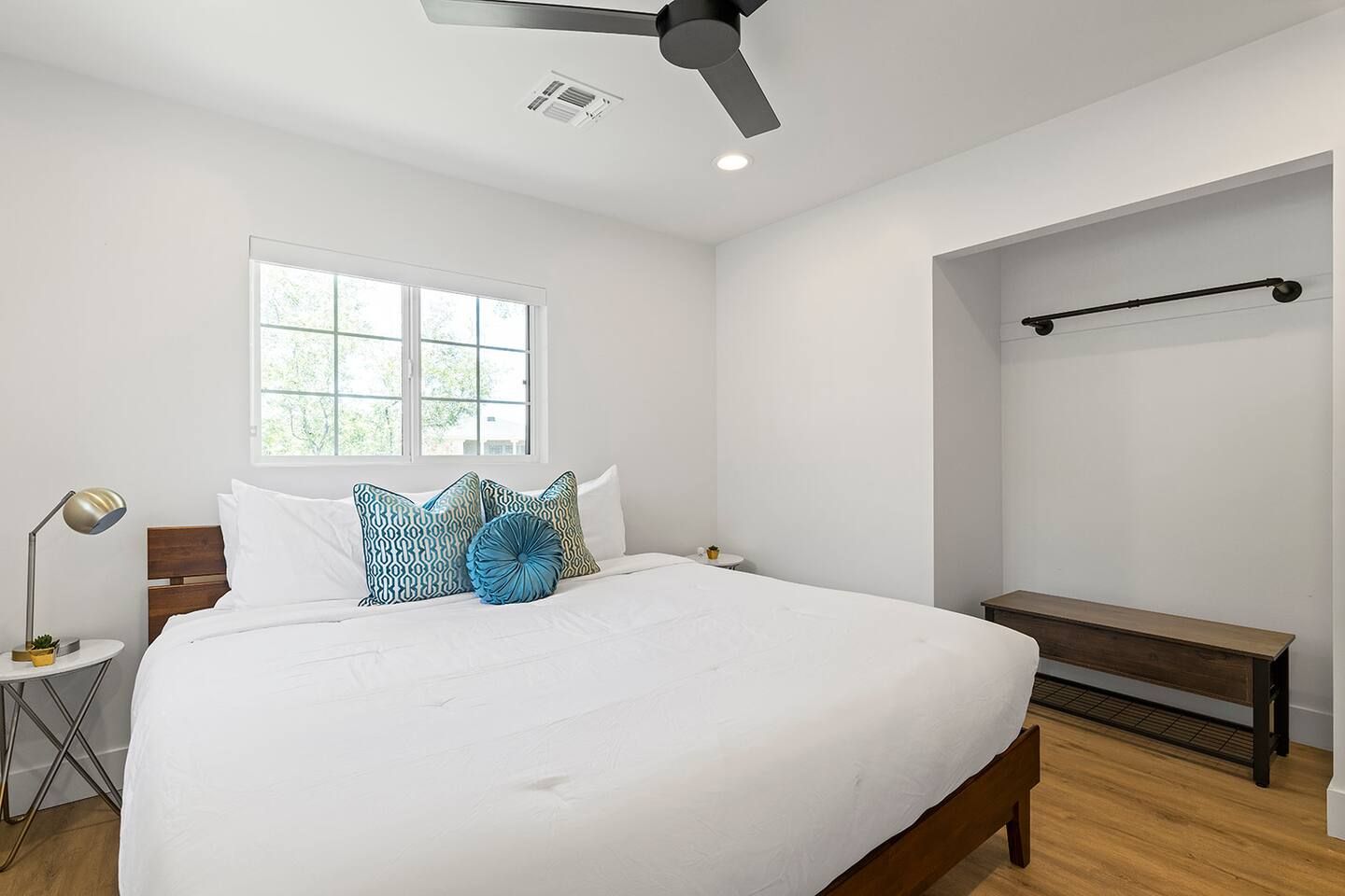 A bedroom with a bed, a bedside table, a lamp, a window, and a ceiling fan.