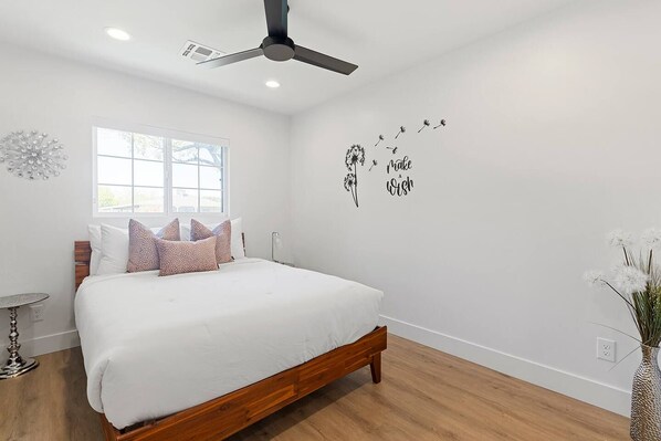 A bedroom with a bed, a ceiling fan, a window, and a wall decoration. - The Elliott at Biltmore | Fire Pit, Grill (Phoenix)