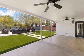 A covered patio with a ceiling fan, a barbecue grill, and a seating area with a sofa and cushions. - The Elliott at Biltmore | Fire Pit, Grill (Phoenix)
