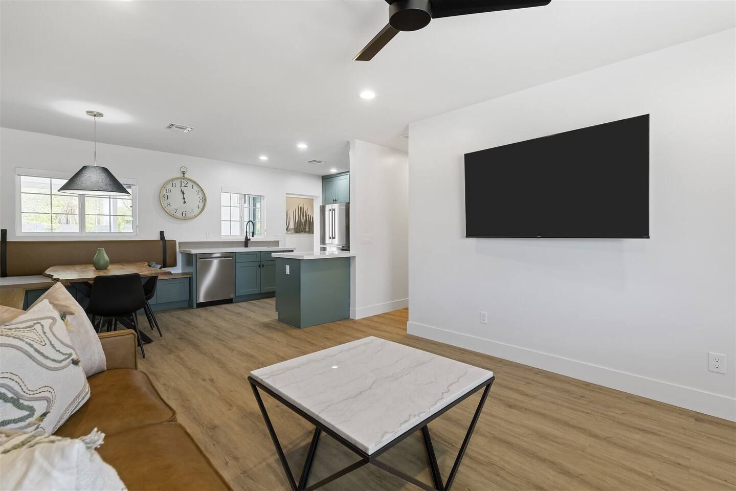 A modern living room with a marble coffee table, a dining area with a bench, and a kitchen with a built-in island.
