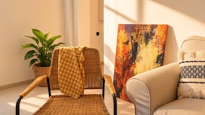 A wicker chair with a checkered throw, a potted plant, a colorful abstract painting, and a sofa with patterned cushions. - 3-Storey Private Townhouse with Sauna,Bar,Terrace, 3BR,3BA (Beyoğlu)