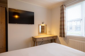 Un dormitorio con una cama, un escritorio de madera con espejo, un televisor de pantalla plana y una ventana con persianas.