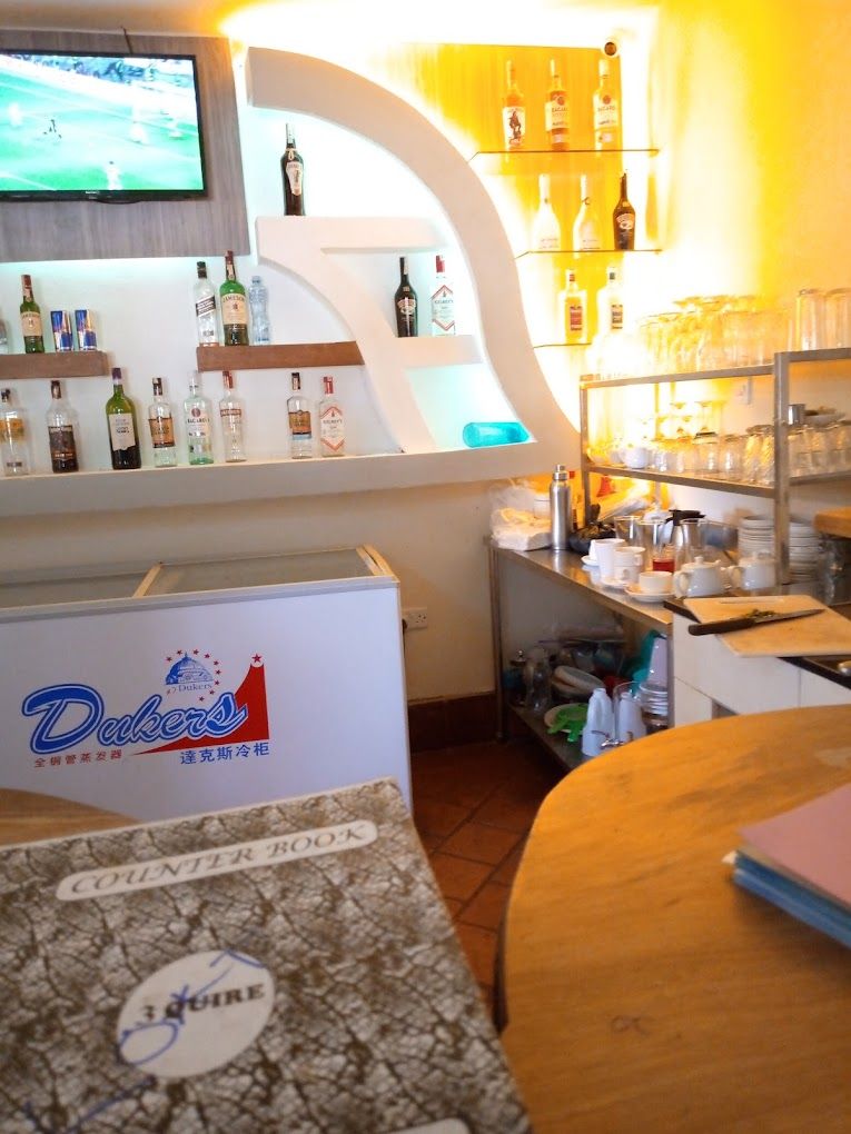 A bar area with shelves of bottles and glasses, a counter with a sign, and a television mounted on the wall.