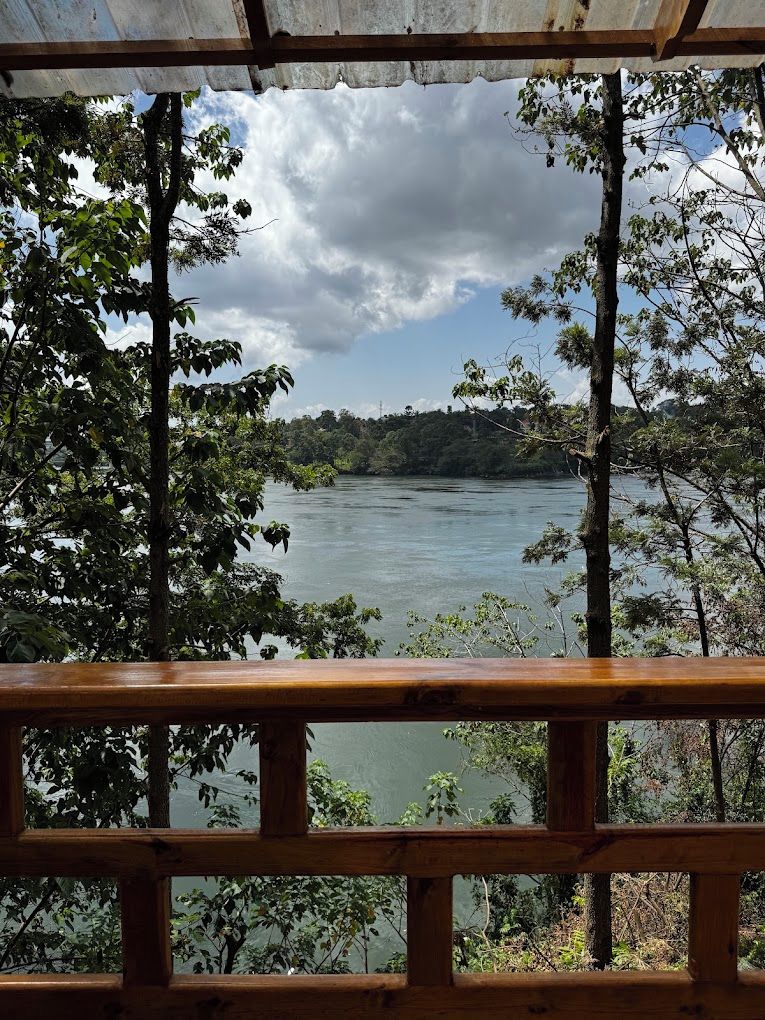 A view from a wooden balcony overlooking a river with trees and a cloudy sky.