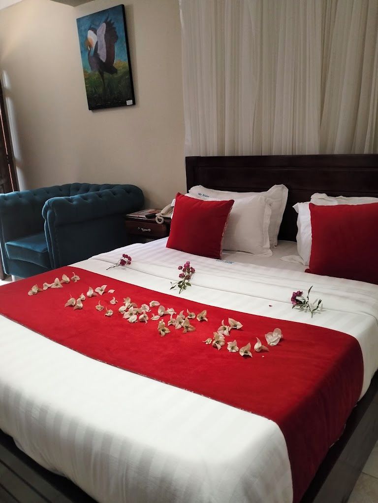 A hotel room with a bed, red and white bedding, a nightstand, and a painting on the wall.