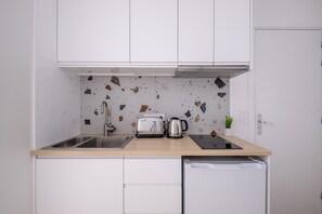 Una cocina con armarios blancos, una encimera, un fregadero, un tostador, una tetera y una pequeña planta en maceta.