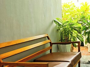 Un banco de madera con asiento acolchado, ubicado frente a una pared lisa y una planta en maceta cerca.