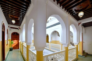 A corridor with arches, a wooden door, and a view of a building with a tiled roof. - Riad DAR ORIANE & SPA (Marrakech)