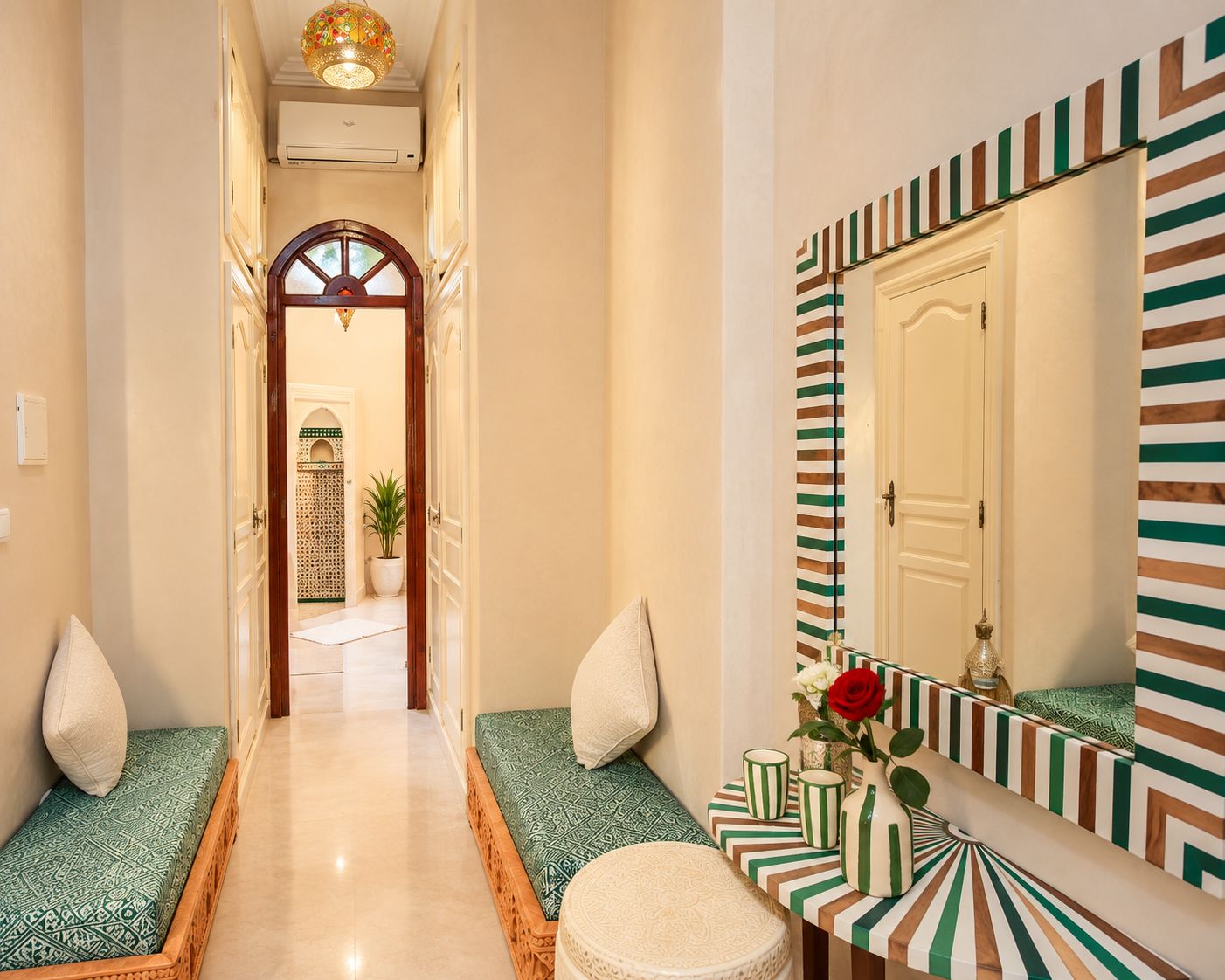 A hallway with a mirrored vanity, a bench, and a door leading to another room.