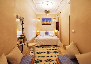 Una habitación de hotel con cama, mesitas de noche, una silla, una alfombra y un cuadro en la pared.