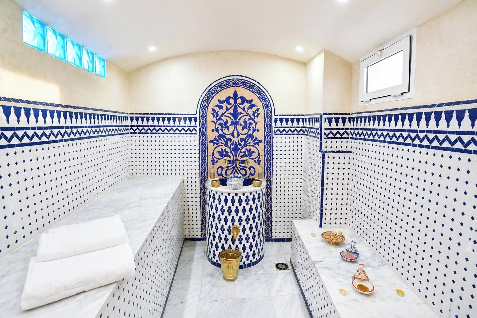 A bathroom with a white and blue patterned tile design, a central decorative column, and a sink with toiletries.