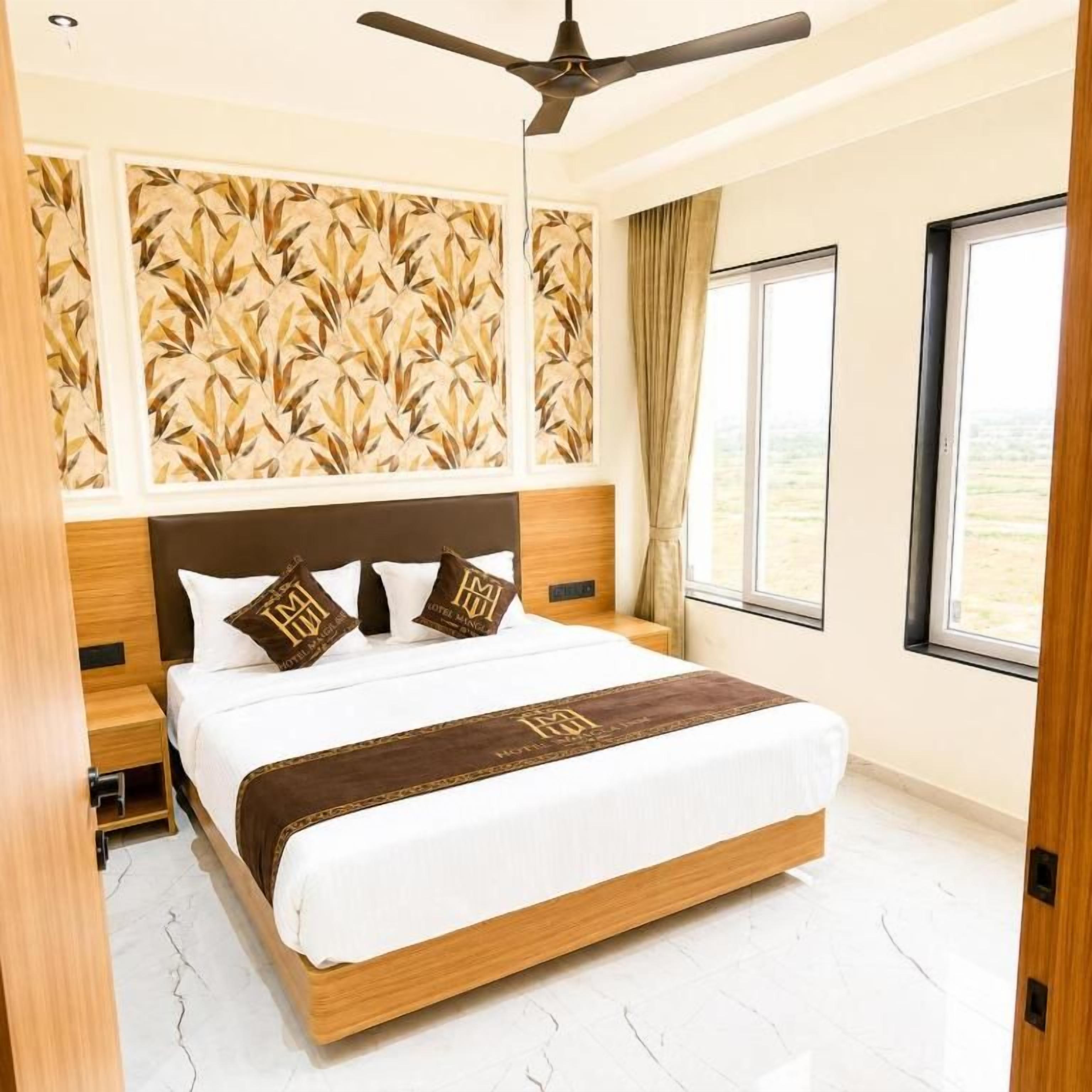 Una habitación de hotel con una cama, un ventilador de techo, una ventana con cortinas y una pared con diseño.
