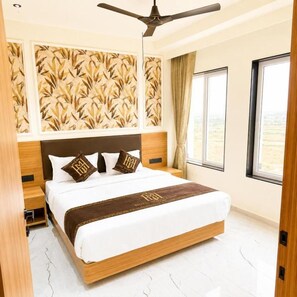 Quarto de hotel com cama, ventilador de teto, janela com cortinas e parede estampada.