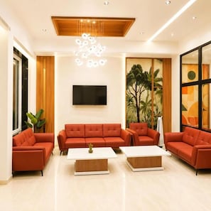 A modern living room with a large sofa set, a flat-screen TV, and a wooden ceiling design.