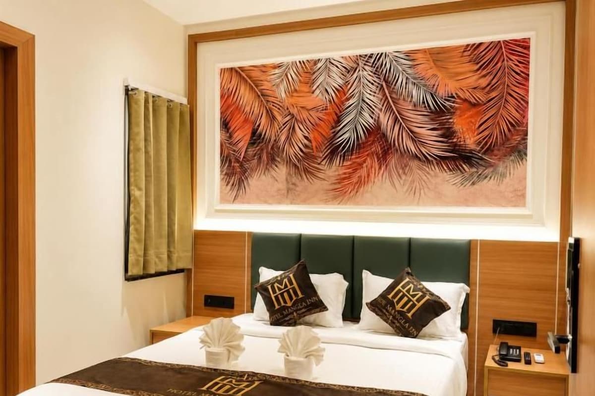 Quarto de hotel com cama, cabeceira, mesa de cabeceira, TV fixada na parede e uma obra de arte emoldurada acima da cama.
