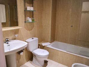 A bathroom with a bathtub, toilet, sink, and a glass shelf with toiletries. - Luxe Duplex Appartement in Marina del Sol, Mijas (Mijas)