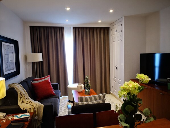 A hotel room with a sofa, a coffee table, a TV, and a large window with curtains. - Luxe Duplex Appartement in Marina del Sol, Mijas (Mijas)