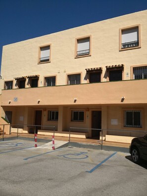 A multi-story building with a flat facade, multiple windows with shutters, and a parking area with a wheelchair-accessible space. - Luxe Duplex Appartement in Marina del Sol, Mijas (Mijas)