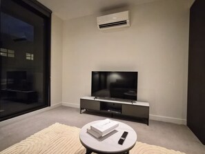 Un salon moderne avec un téléviseur à écran plat posé sur un meuble, une télécommande et un livre sur une petite table.