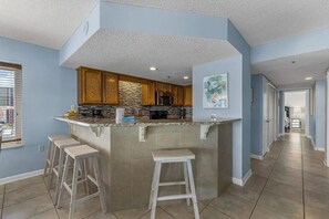 A kitchen with a bar area, wooden cabinets, and a stone backsplash. - 3BR Beachfront condo w/ Gulf views, pools, hot tub and direct beach access (Orange Beach)