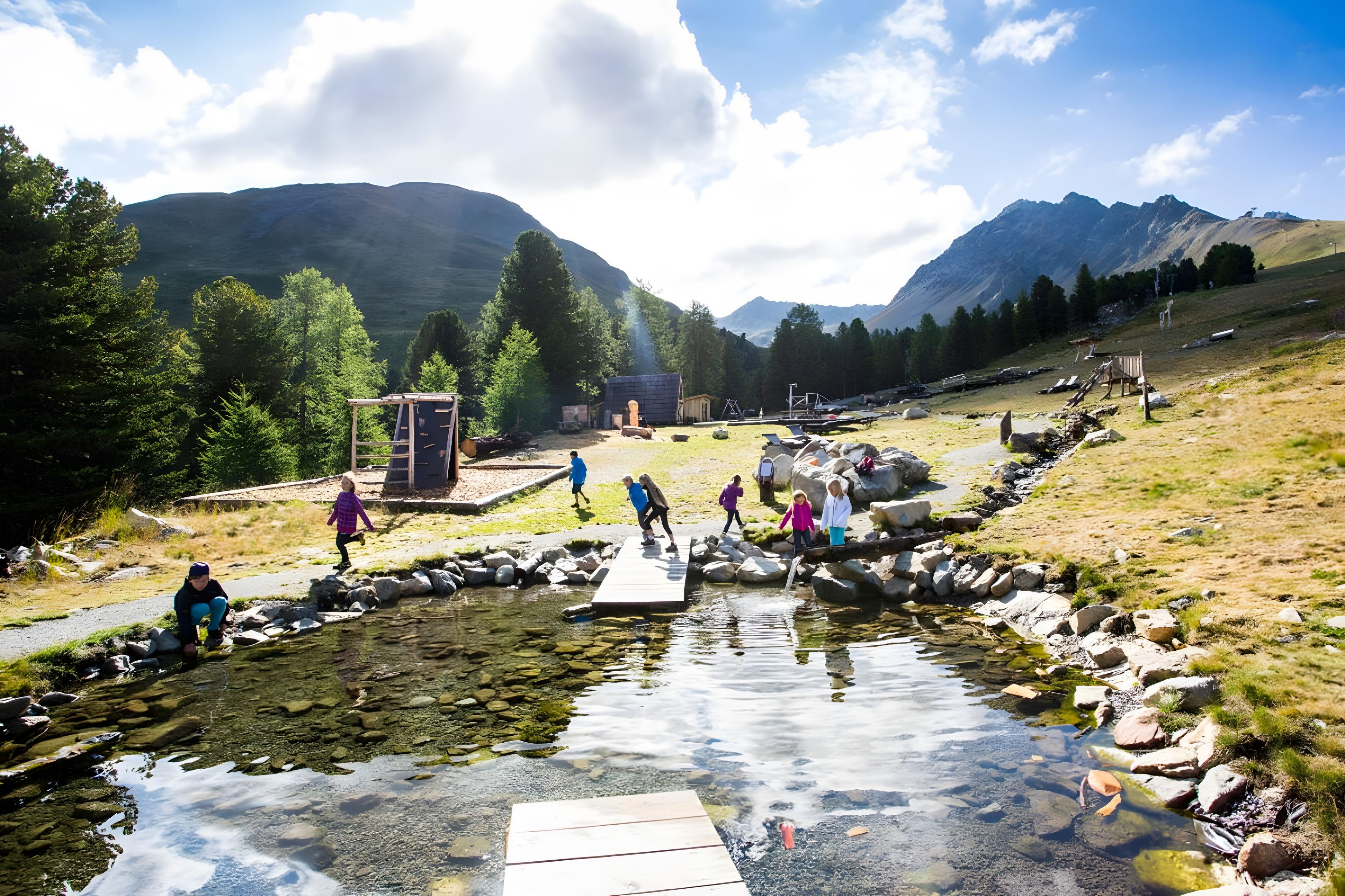 A natural landscape with a clear stream, rocky terrain, and mountains in the background.