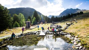 A natural landscape with a clear stream, rocky terrain, and mountains in the background.