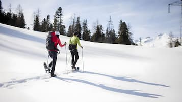 Duas pessoas fazem caminhada em uma encosta coberta de neve, com árvores ao fundo.