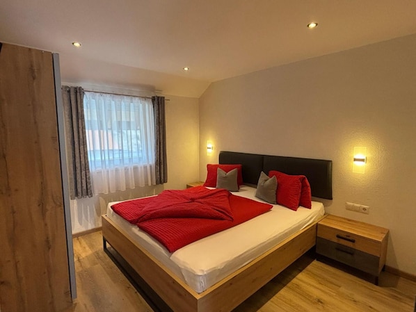 A bedroom with a wooden bed, a nightstand, and a window with curtains.