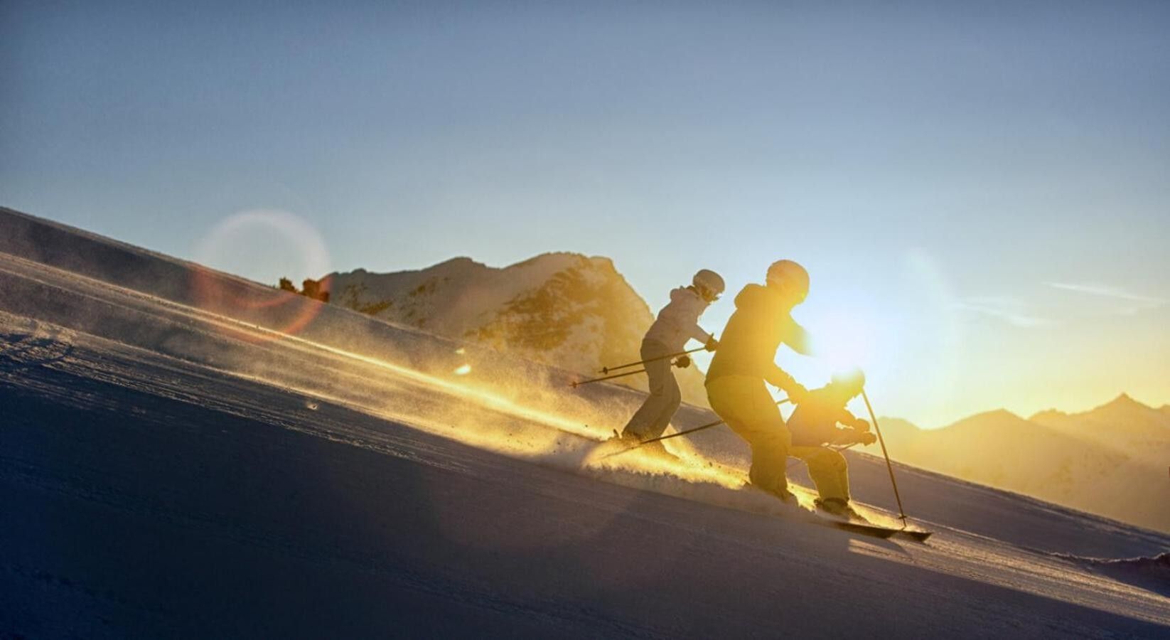 A ski slope with skiers in motion, mountains in the background, and a clear sky.