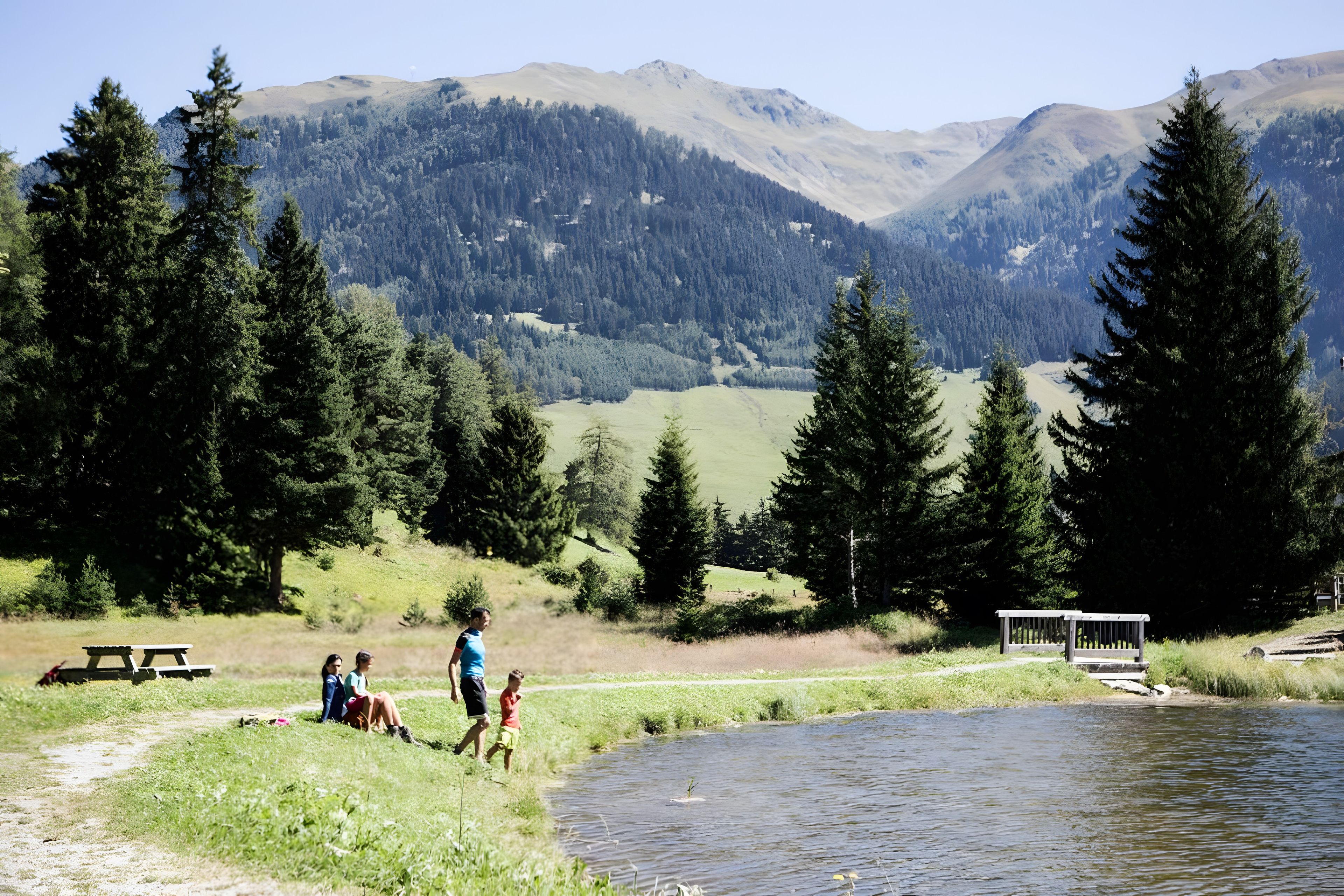 Un cadre agréable au bord du lac, avec des tables de pique-nique, un banc et une vue sur les montagnes.