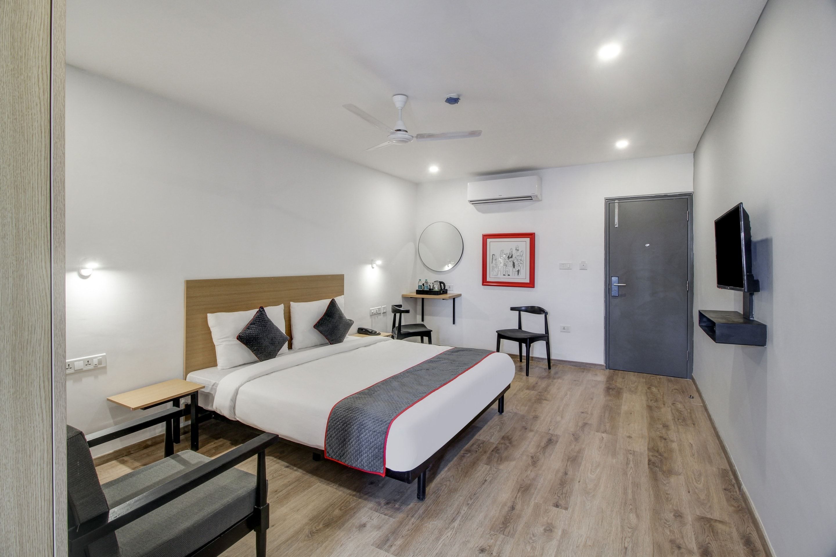 A hotel room with a bed, bedside table, chair, desk, and a TV mounted on the wall.