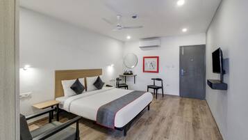 A hotel room with a bed, bedside table, chair, desk, and a TV mounted on the wall.