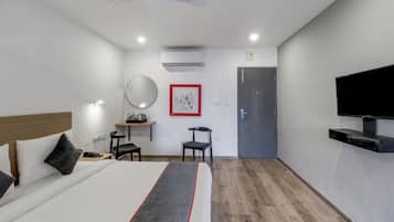A hotel room with a bed, a desk, a chair, a television, and a door.