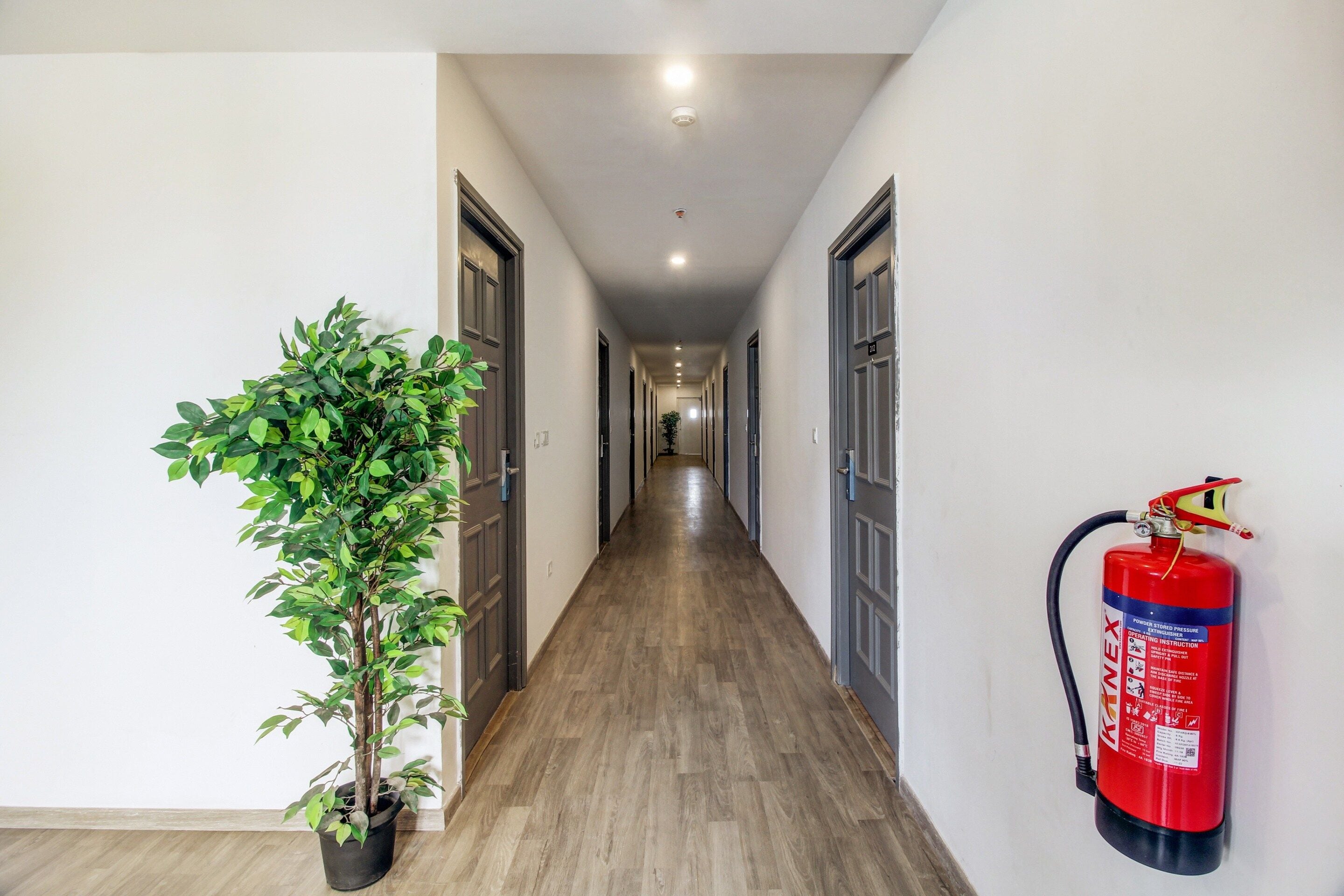 A hallway with wooden flooring, doors on both sides, and a fire extinguisher mounted on the wall.
