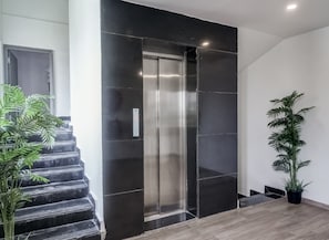 A modern elevator with a metallic finish, flanked by black-tiled walls and wooden flooring.