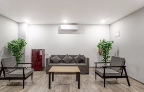 A modern living room with a grey sofa, two armchairs, a wooden coffee table, a red refrigerator, and two potted plants. - Super Townhouse RCC Majestic 397 (Hyderabad)