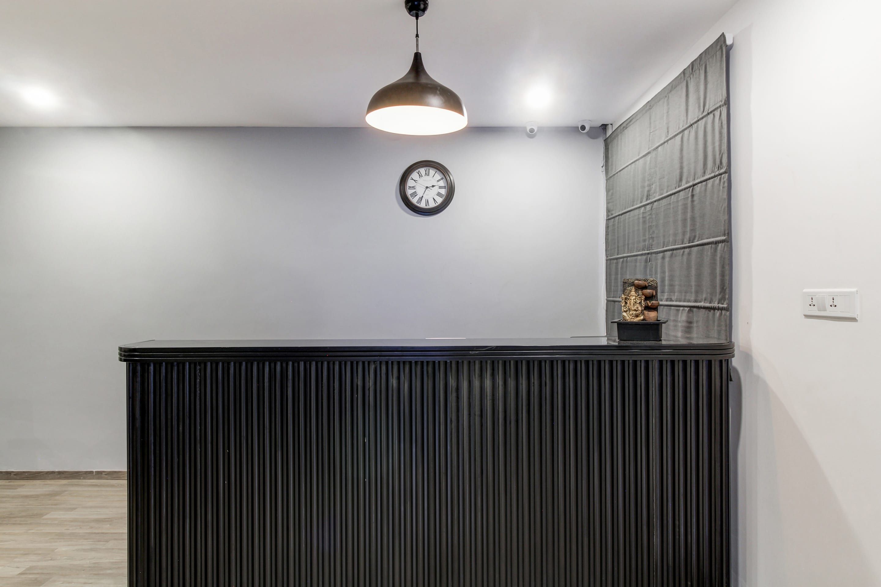 A reception desk with a clock above it, a pendant light, and a small statue on the wall.