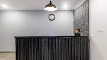 A reception desk with a clock above it, a pendant light, and a small statue on the wall.