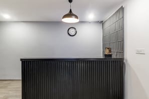 A reception desk with a clock above it, a pendant light, and a small statue on the wall.