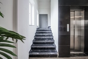 Una escalera que lleva a una puerta, con un moderno ascensor a la derecha.