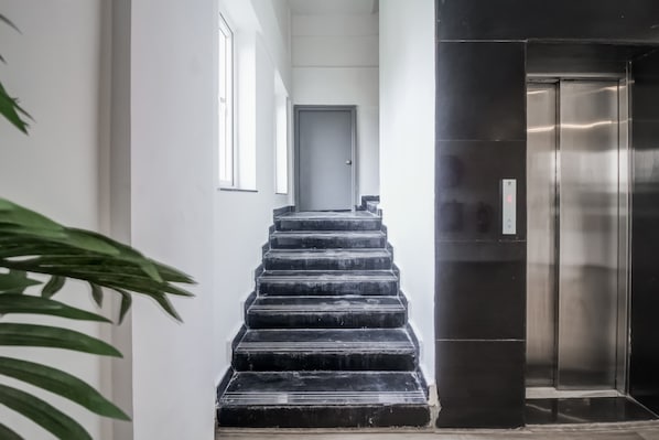 A staircase leading to a door, with a modern elevator on the right. - Super Townhouse RCC Majestic 397 (Hyderabad)